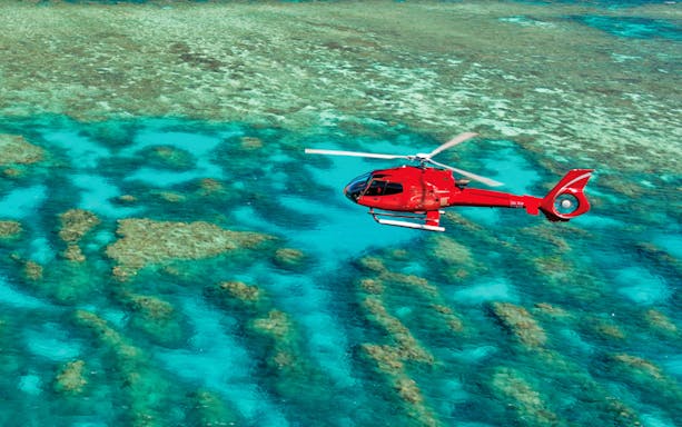 Red helicopter flying over the Great Barrier Reef's turquoise waters.
