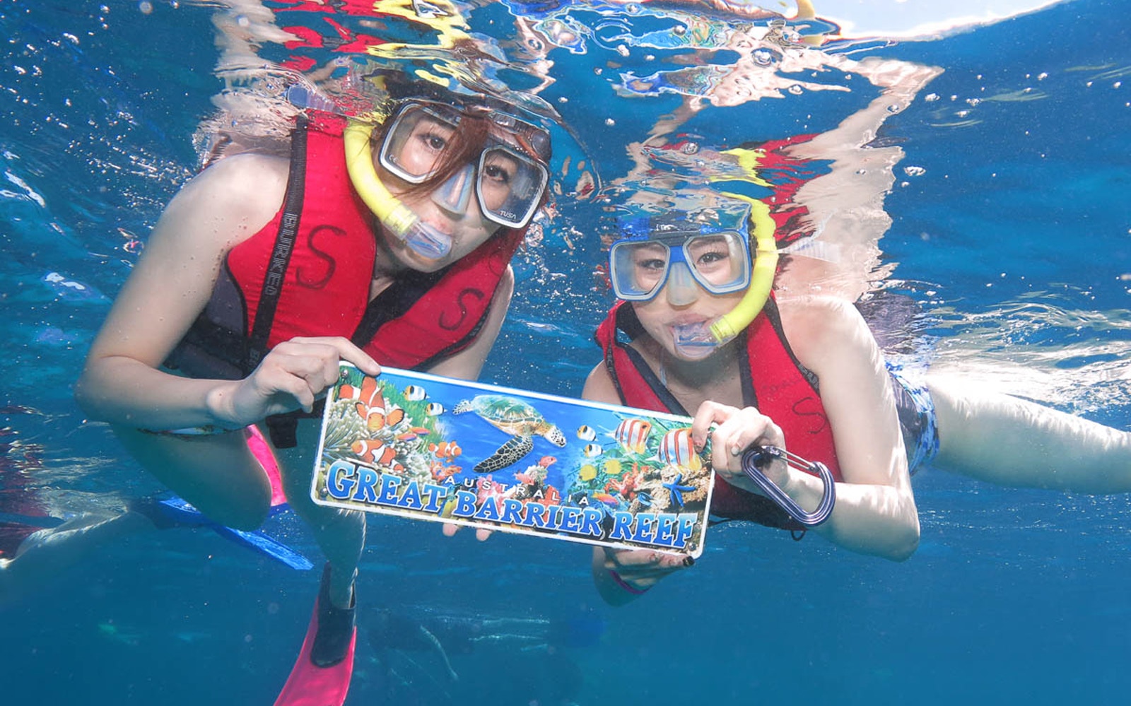 Snorkelers holding Great Barrier Reef sign underwater during adventure cruise.