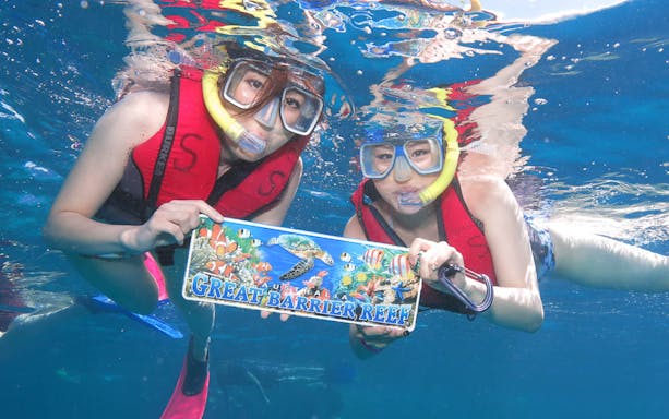 Snorkelers holding Great Barrier Reef sign underwater during adventure cruise.