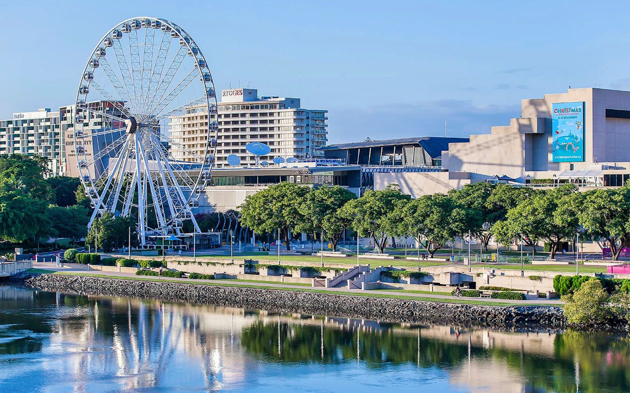 Ferris wheel by the Brisbane River with city buildings in the background.