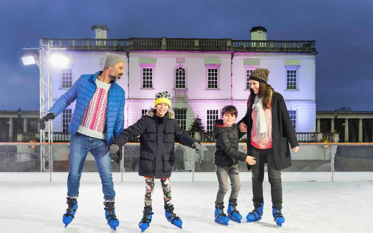 Family ice skating at The Queen's House Ice Rink, London, with illuminated building backdrop.