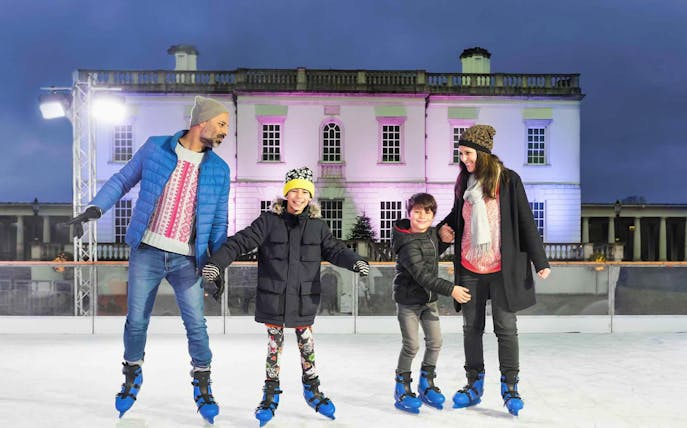Family ice skating at The Queen's House Ice Rink, London, with illuminated building backdrop.