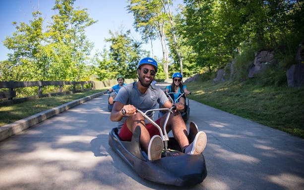 People riding luge carts on a scenic track surrounded by trees at Sentosa.