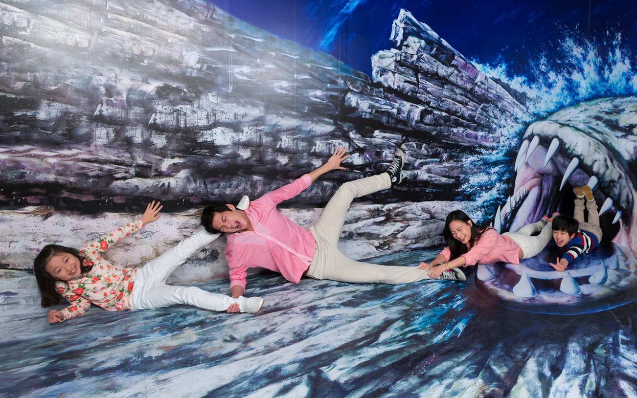 Family posing in front of a 3D art mural at Sentosa, Singapore, depicting a shark attack.