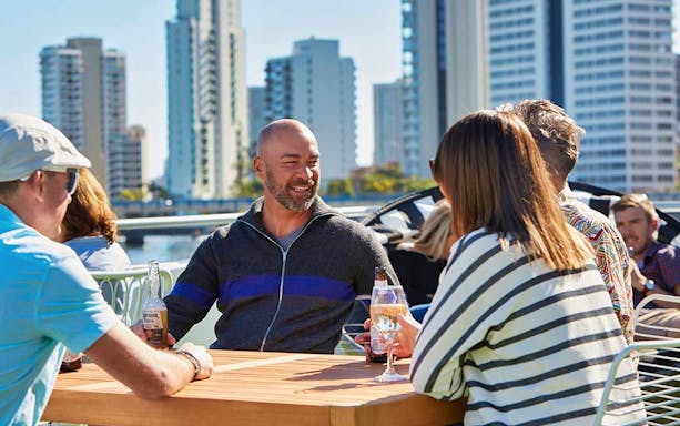 Group enjoying drinks on a Sea World sightseeing cruise with city skyline in the background.