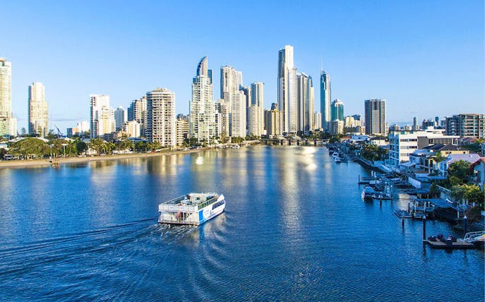 Cruise boat on Gold Coast waterway with city skyline in background.