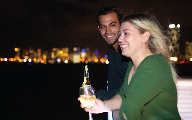 Couple enjoying drinks on a Sea World dinner cruise with city lights in the background.