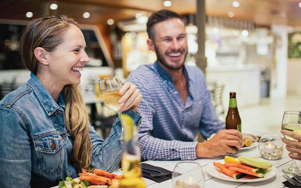 Guests enjoying dinner and drinks on a Sea World cruise with live entertainment.