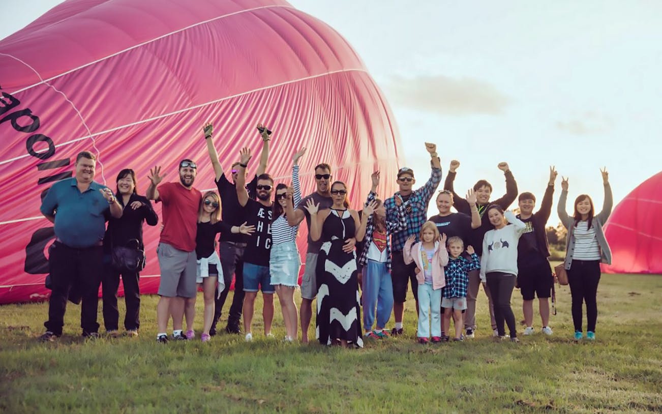 Group celebrating in front of a pink hot air balloon before a 60-minute ride.