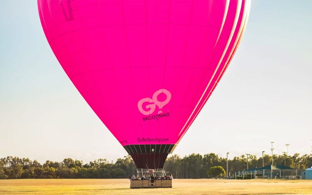 Hot air balloon preparing for flight with passengers in a field, Go Ballooning logo visible.