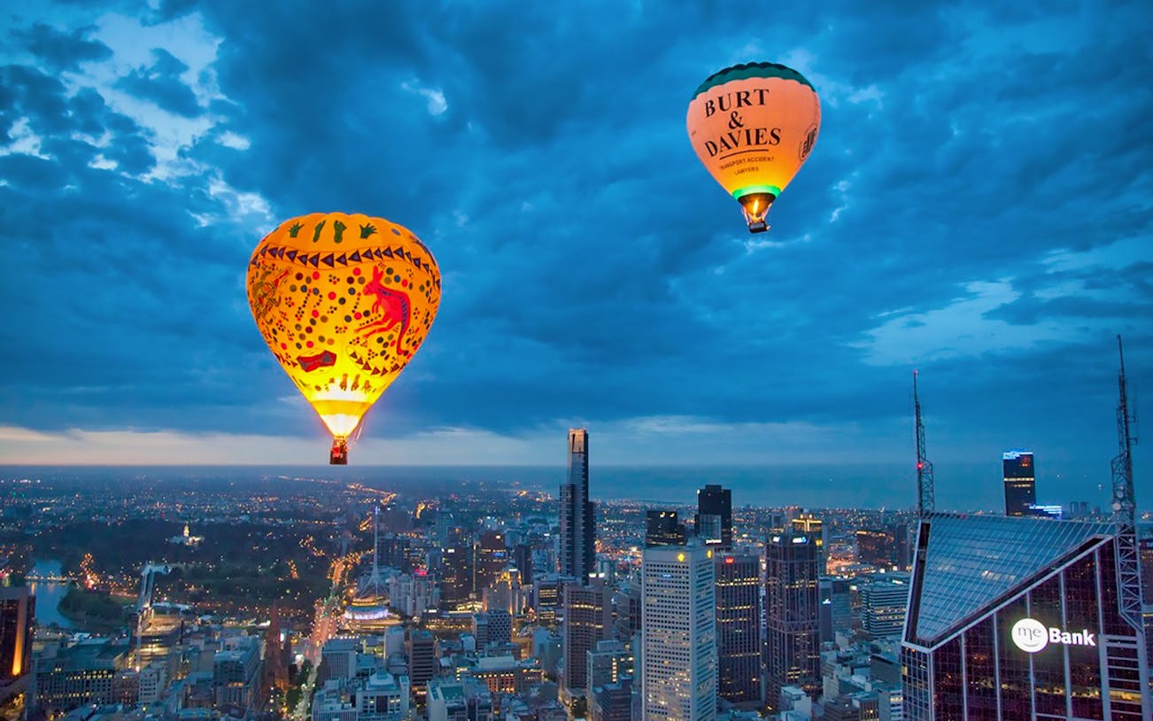Hot air balloons over Melbourne skyline at sunrise.