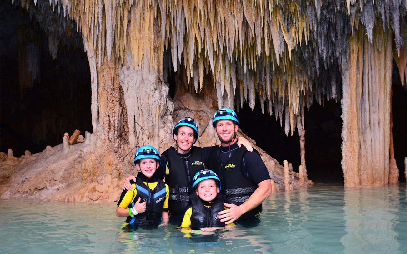 Family exploring Rio Secreto underground river with stalactites in background.