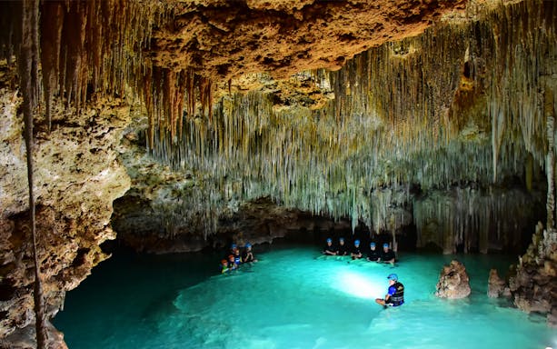 Visitors exploring Rio Secreto's underground river with stalactites in Mexico.