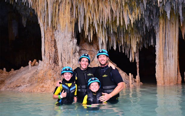 Family exploring Rio Secreto Underground River with stalactites in background.