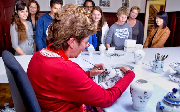 Artisan painting pottery at Royal Delft Blue Factory with visitors observing.