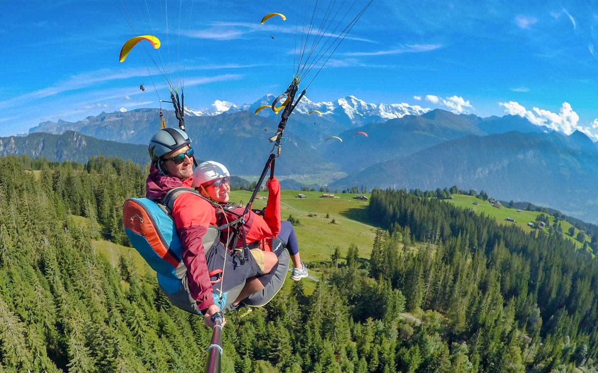 Paragliding over Interlaken with views of the Swiss Alps and lush green forests.