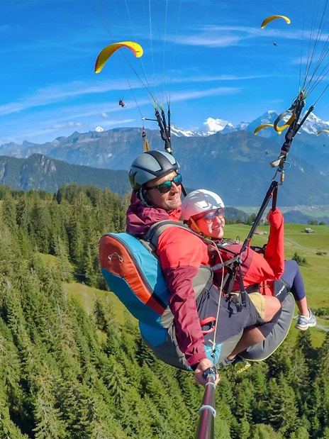 Paragliding over Interlaken with views of the Swiss Alps and lush green forests.