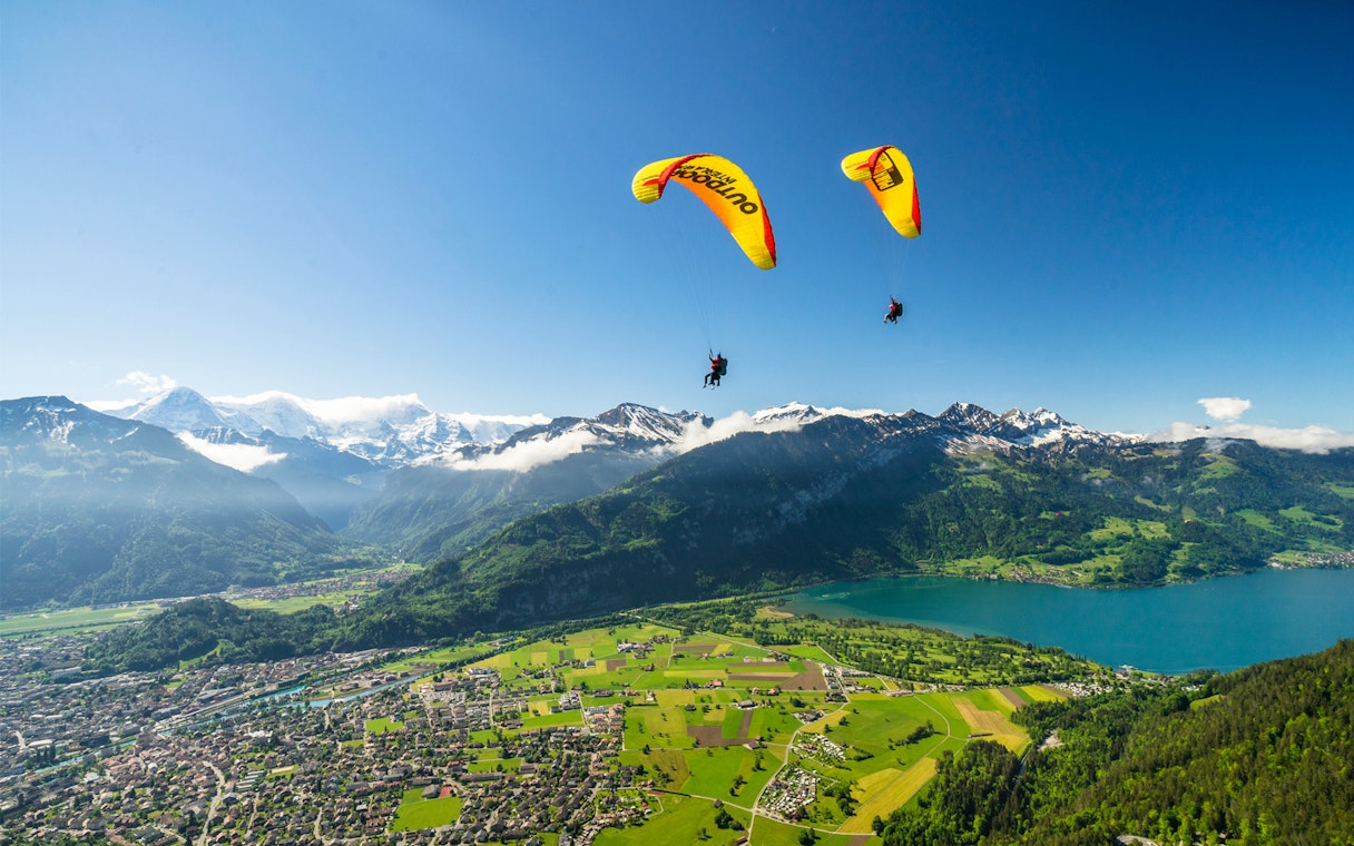 Paragliders soaring over Interlaken with views of mountains and Lake Thun.