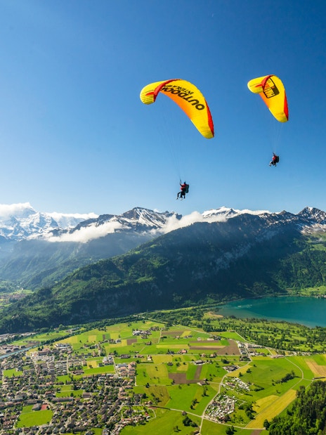 Paragliders soaring over Interlaken with views of mountains and Lake Thun.