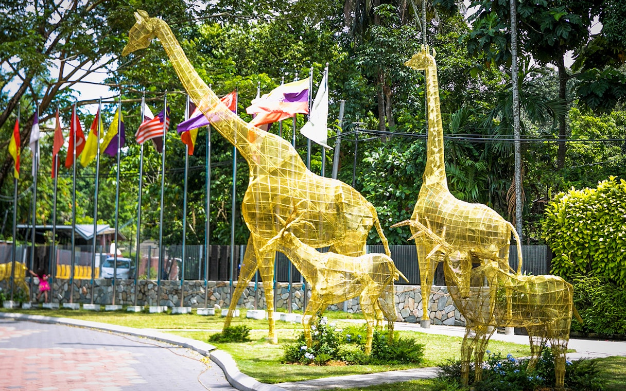 Golden giraffe sculptures at Zoo Negara entrance, Kuala Lumpur, with flags in the background.