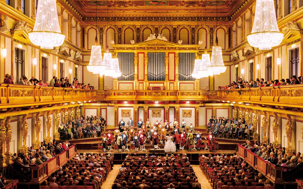 Mozart Orchestra performing at Wiener Musikverein, Vienna, with audience in ornate concert hall.