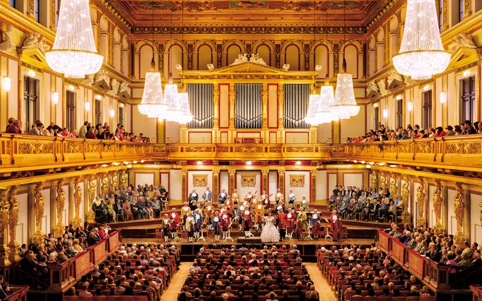Mozart Orchestra performing at Wiener Musikverein, Vienna, with audience in ornate concert hall.