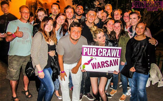 Group of people holding a "Pub Crawl Warsaw" sign during a night event.