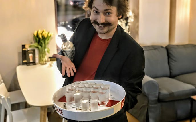 Man holding a tray of vodka shots in a cozy Warsaw setting.