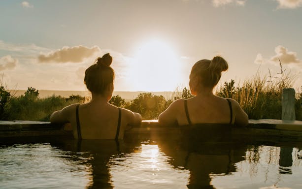Two people relaxing in a hot spring at sunrise, Mornington Peninsula Hot Springs.