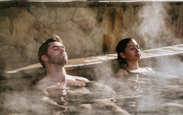 Couple relaxing in steaming hot spring pool at Mornington Peninsula Bath House.