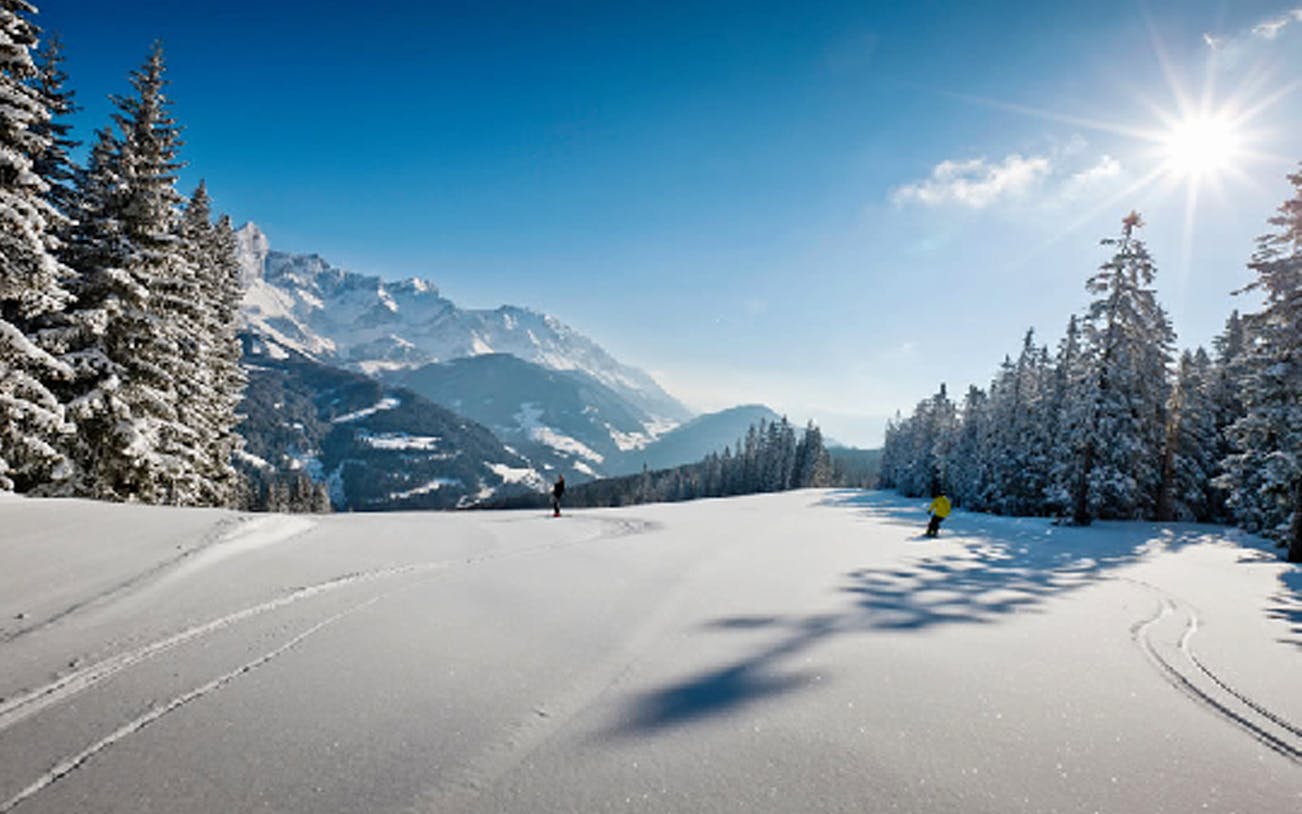 Skiers on a snowy slope with mountains in the background at Ski Amade, Austria.