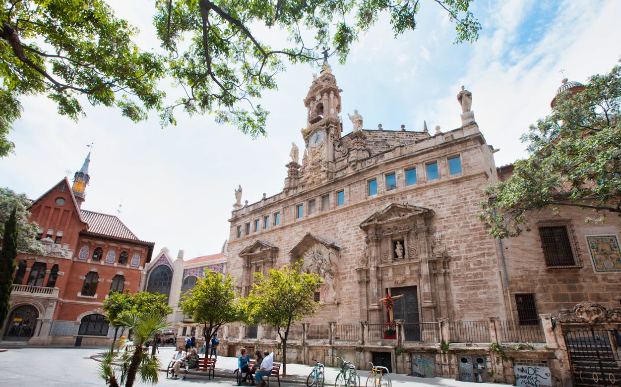 Santos Juanes Church facade in Valencia, Spain, with people sitting nearby.