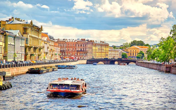 River cruise boat on a canal with historic buildings and a bridge in the background.