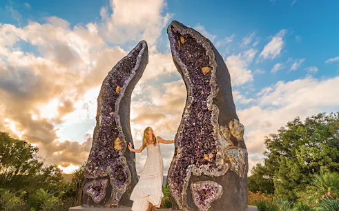 Woman standing between large amethyst geodes at Crystal Castle, Byron Bay.