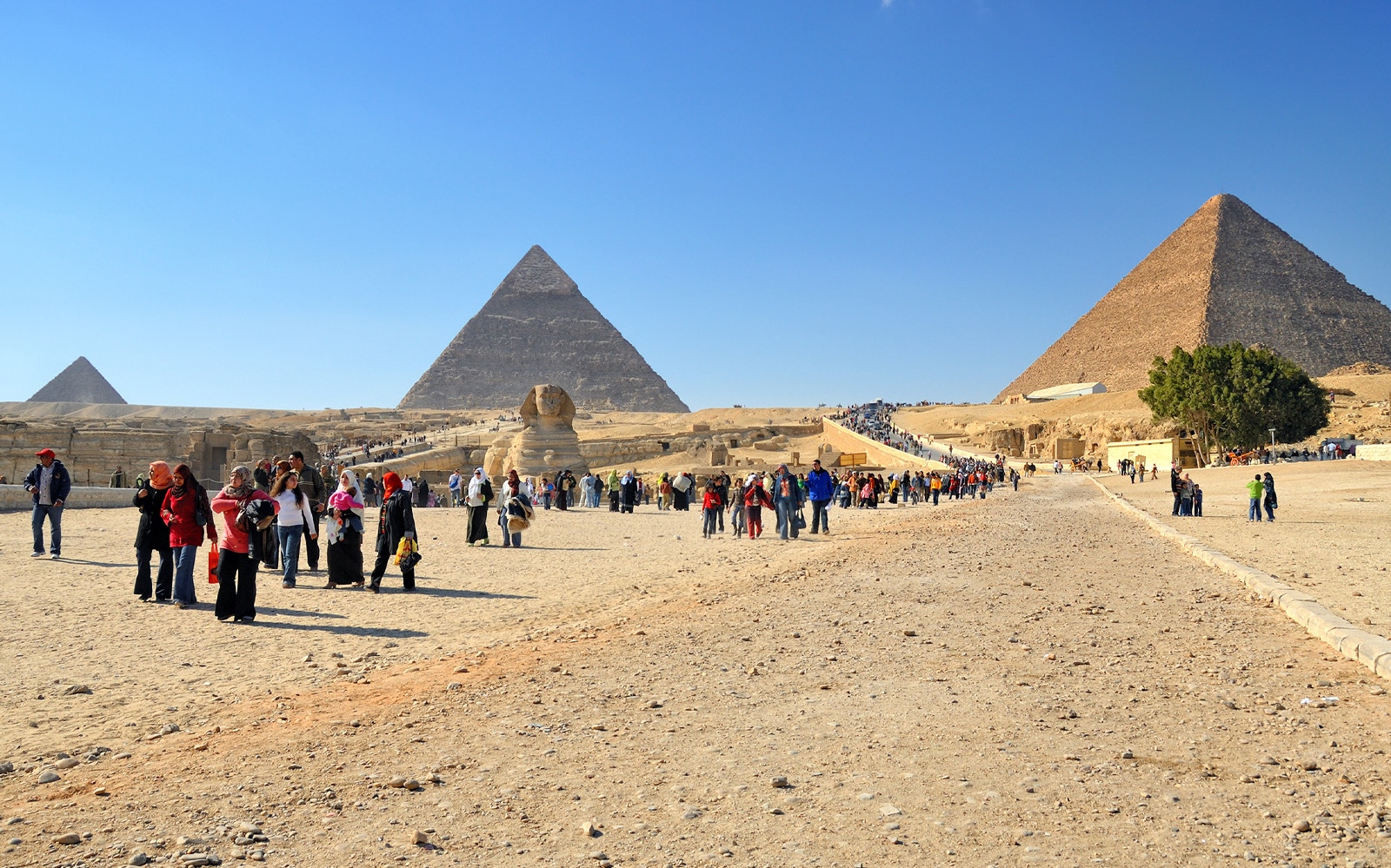 Tourists exploring the Pyramids of Giza with the Sphinx in view.