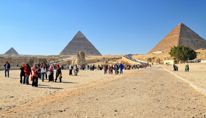 Tourists exploring the Pyramids of Giza with the Sphinx in view.