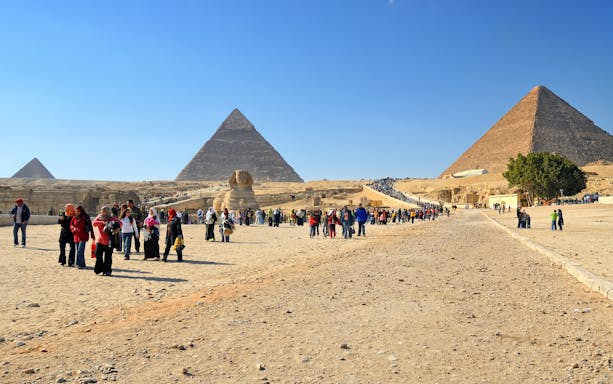 Tourists exploring the Pyramids of Giza with the Sphinx in view.