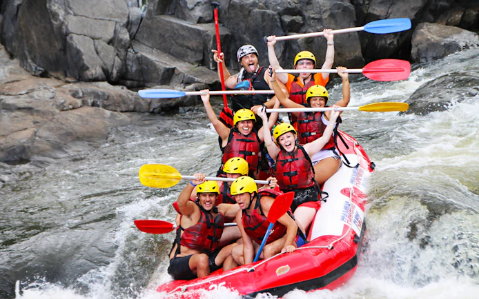Group rafting on Barron River, navigating rapids with paddles raised, wearing helmets and life vests.