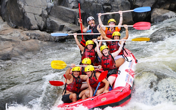 Group rafting on Barron River, navigating rapids with paddles raised, wearing helmets and life vests.