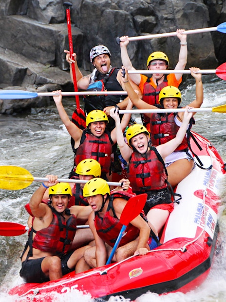 Group rafting on Barron River, navigating rapids with paddles raised, wearing helmets and life vests.