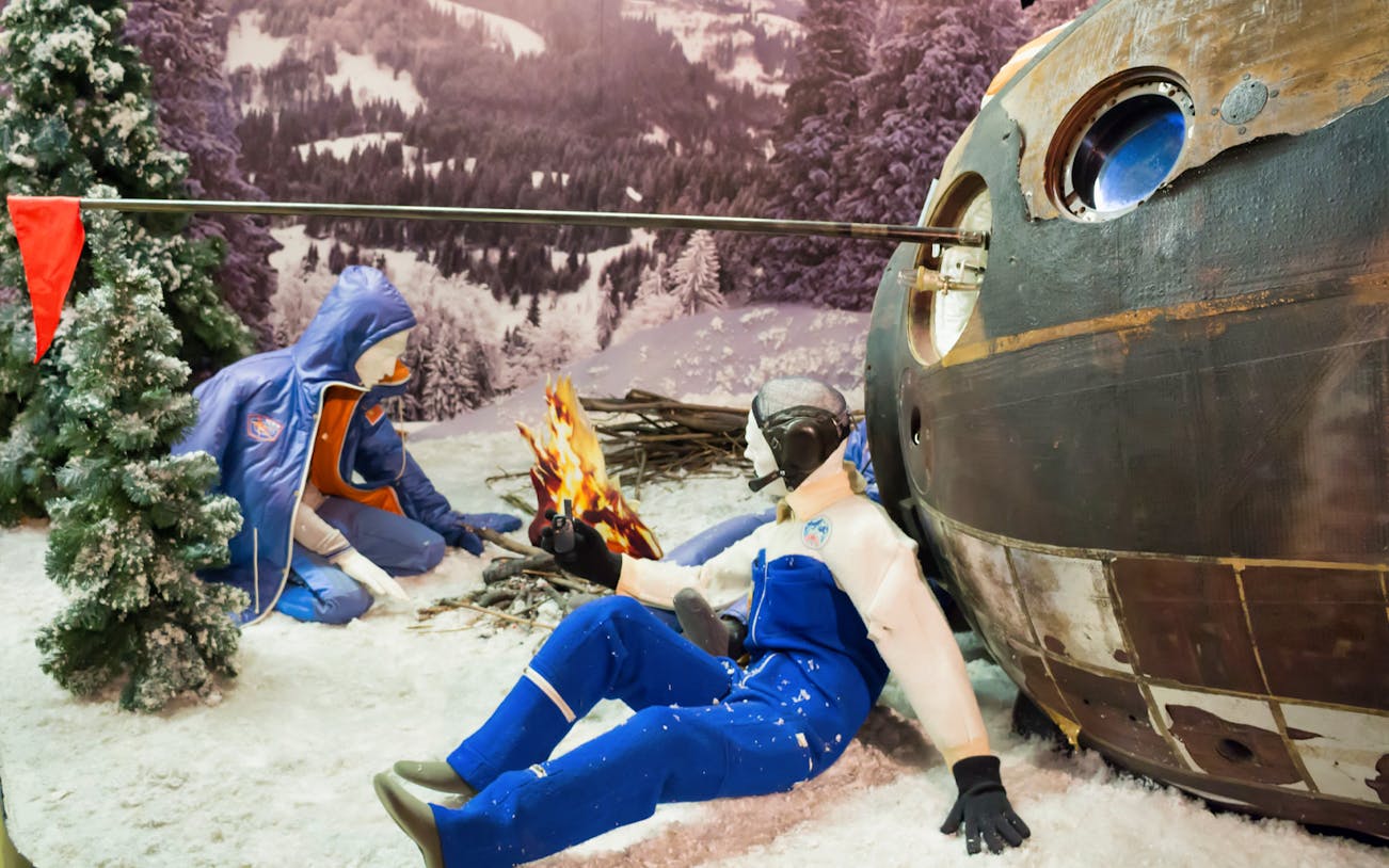 Astronaut mannequins in winter gear beside a space capsule at the Space Museum.