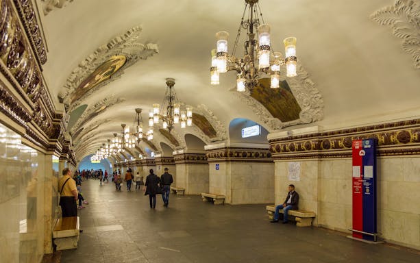 Moscow Metro station with ornate chandeliers and decorative arches on a guided tour.