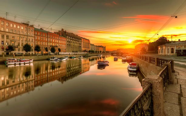 Canal view at sunset in St. Petersburg, Russia, with boats and historic buildings.