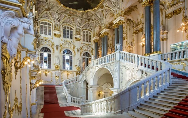 Grand staircase in the Hermitage Museum, St. Petersburg, with ornate gold detailing.