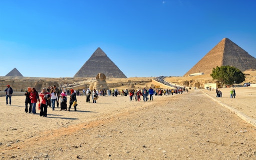 Tourists exploring the Pyramids of Giza and the Sphinx on a sunny day in Egypt.