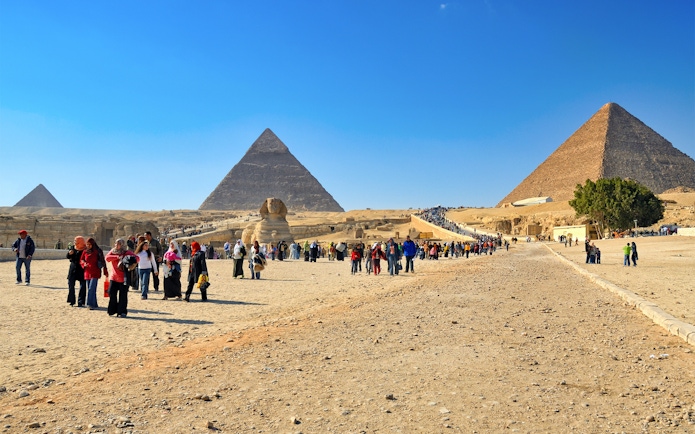 Tourists exploring the Pyramids of Giza and the Sphinx on a sunny day in Egypt.