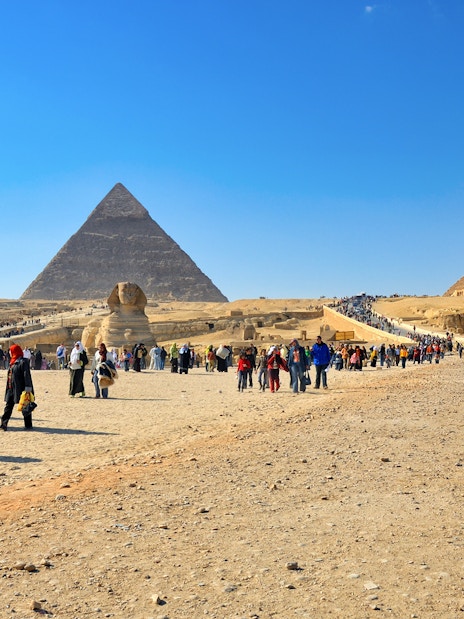 Tourists exploring the Pyramids of Giza and the Sphinx on a sunny day in Egypt.