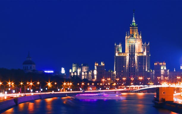 Moscow skyline at night with illuminated skyscraper and river during city walking tour.