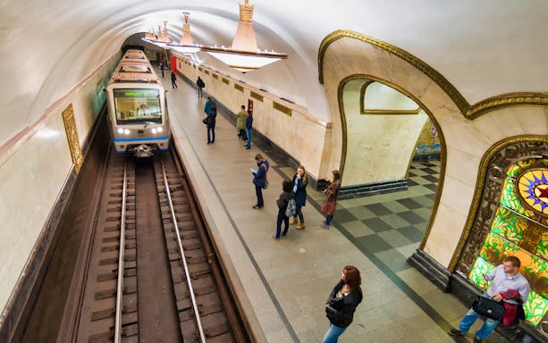 Moscow metro station with train arriving and people waiting on the platform.