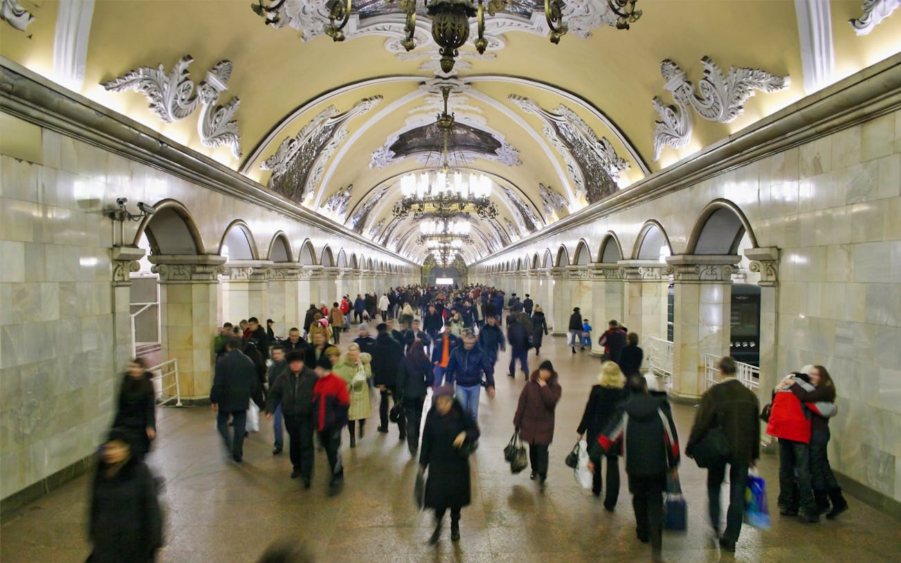Moscow metro station with ornate ceiling and people walking during a guided night tour.